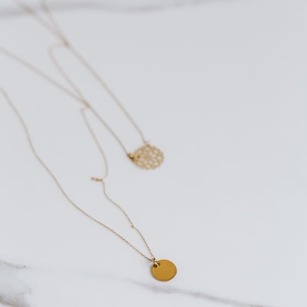 The uploaded photo of two fine gold pendant necklaces laid flat on white marble.